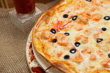 pizza thin olives, shrimps, crabs, seafood, on a wooden stand with tomato juice in a glass sink. Cherry tomatoes and sweet peppers, lettuce leaves. Close-up