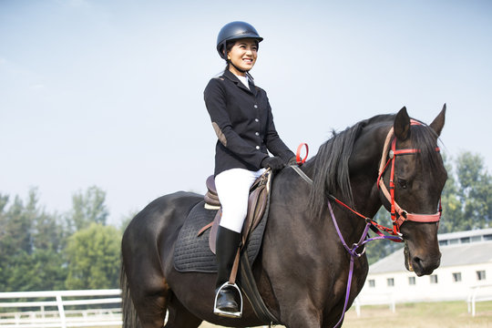 Cheerful young Chinese woman riding horse 