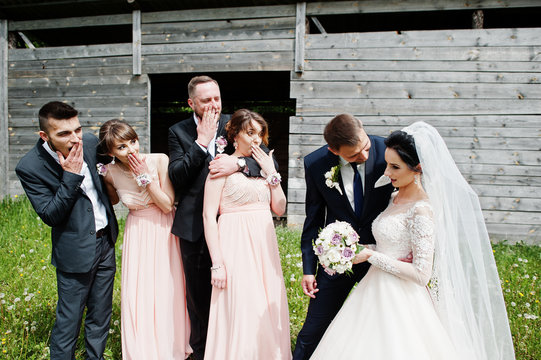 Bridesmaids with groomsmen and wedding couple having fun outdoors next to the old rustic wooden barn.