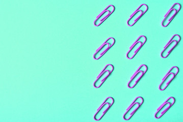 Violet paper clips isolated on turquois background, close up, copy space. Top view, flat lay. Back to school, college, education concept