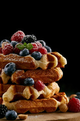delicious stacked belgian waffles with berries on wooden cutting board on black