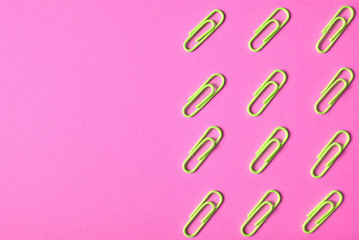 Lime green paper clips isolated on pink background, close up, copy space. Top view, flat lay. Back to school, college, education concept