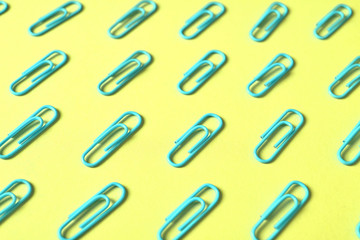 Blue paper clips isolated on yellow background, close up, copy space. Top view. Back to school, college, education concept