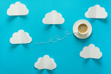 Coffee cup in shape of balloon with clouds on blue paper background.