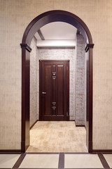 Fototapeta premium Passage through wooden archway into corridor with entrance door tiked in brown tones