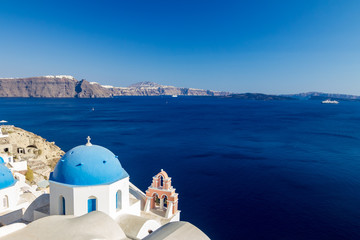 Incredibly romantic scene on Santorini. Fira, Greece. Amazing daytime view towards the deep sea crystal waters with white houses and blue church roof with white Christian cross and bells