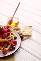tasty belgian waffles with berries and glass of honey on white wooden table