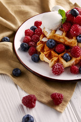 fresh belgian waffles with berries and ice cream on white wooden table