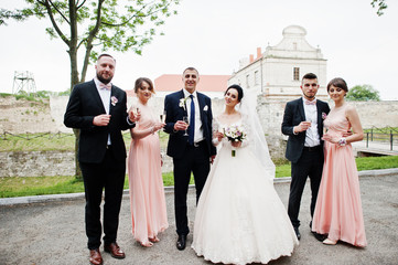 Wedding couple and groomsmen with bridesmaids drinking champagne in the park.