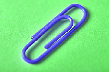 One blue paper clip isolated on green background, close up, copy space. Top view, flat lay. Back to school, college, education concept