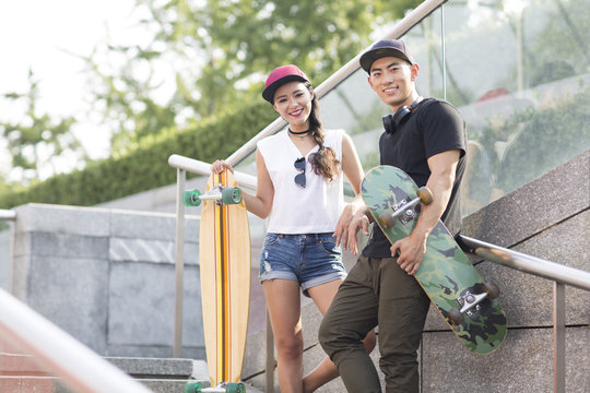 Portrait of cheerful young Chinese couple with skateboard 