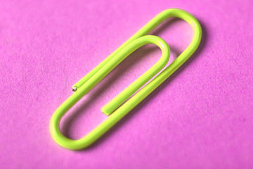 One yellow paper clip isolated on violet background, close up, copy space. Top view, flat lay. Back to school, college, education concept