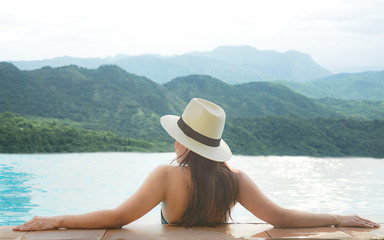 Rear view of happy lifestyle women relax and enjoy in the pool looking at mountain landscape.  Women together on summer and vacations travel to luxury resort. Summer and Holiday Concept