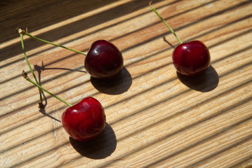 Three cherry berries on a wooden background with light through the window