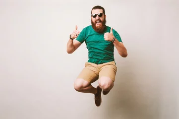 Tuinposter Cheerful bearded hipster man with sunglasses jump over white background and showing thumbs up © Vulp