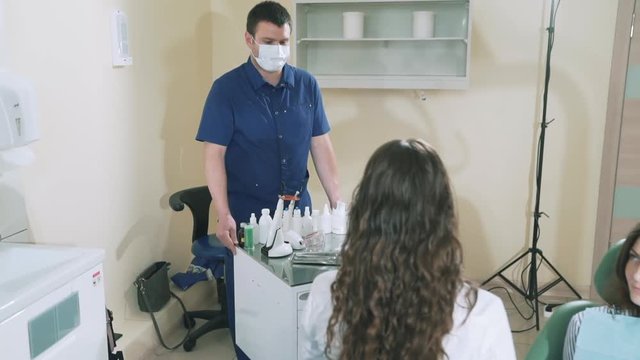delayed shooting steadikam the assistant of the doctor of the stomatologist brings the cart with the equipment to the doctor's office. A female dentist takes a somatic mirror and an ironing pad to