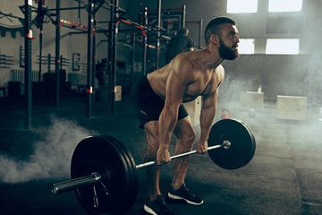 Fit young man lifting barbells working out in a gym