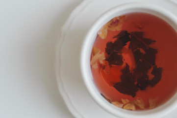 Red hibiscus tea mixed with green tea and rose petals and served in white cup, top view