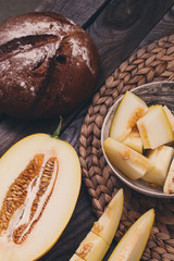 Flat lay rustic composition on retro straw stand sliced melon and dark brown home made bread.