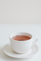 Cup of red herbal tea on white table, vertical photo. Hibiscus tea with rose petals flavor