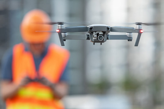 Young Asian engineer flying drone over construction site. Using unmanned aerial vehicle (UAV) for land and building site survey in civil engineering project.