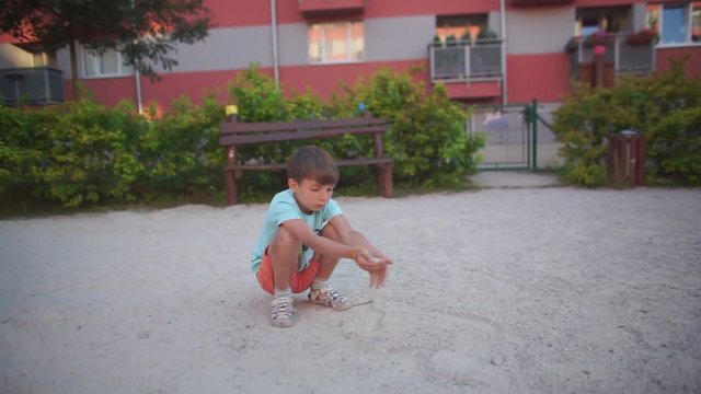 Home education. Quarantine viral infection COVID 19. Self isolation. Social distance.  The boy of 7 years poured palms on a palm sand in a court yard of an apartment house.