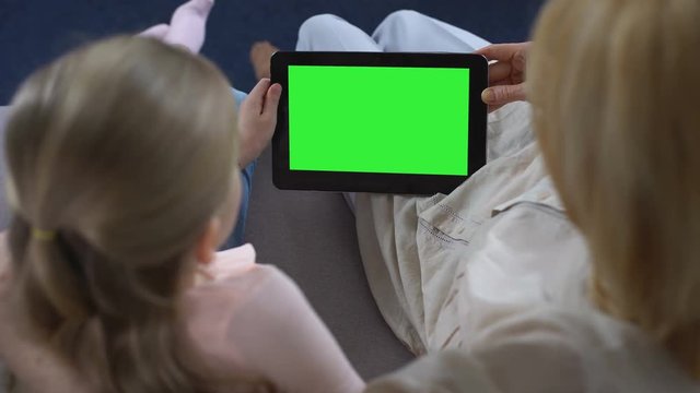 Old woman and little girl hands holding tablet with green screen, watching video