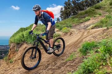 Male mountain biker on a black ebike driving downhill a dirt-track on a mountain in Spain
