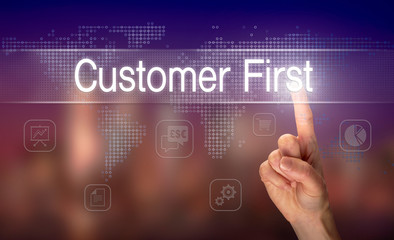 A hand selecting a Customer First business concept on a clear screen with a colorful blurred background.