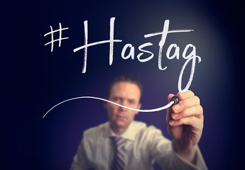 A businessman writing a hashtag concept with a white pen on a clear screen.