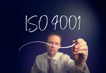A businessman writing a iso 9001 concept with a white pen on a clear screen.