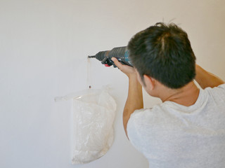 An electric drill being used by Asian handy man drilling into concrete wall