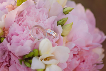 Fototapeta na wymiar White gold wedding rings with stones on a pink wedding bouquet