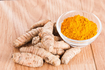 Turmeric powder and fresh turmeric on wooden background