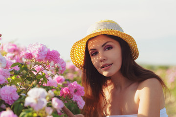 Beautiful young woman posing near roses in a garden.