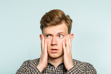 puzzled confused bewildered shocked amazed man clutching his face. portrait of a young guy on light background. emotion facial expression and feelings concept.