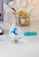 Dropper colorful liquids put in glass conical flasks on the white table in the laboratory