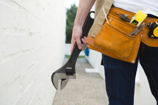 Male carpenter with tool belt holding wrench