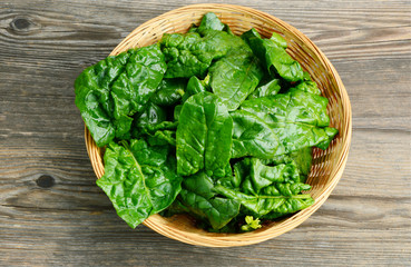 Benefits of Spinach leaves in basket on wooden floor.