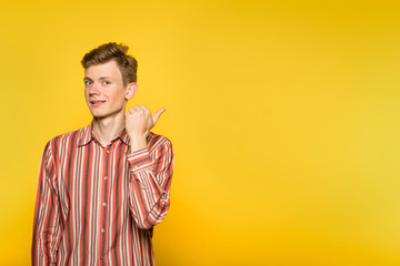 look there. handsome smiling man pointing sideways with a hand. portrait of a young guy on yellow background. free space for advertisement.