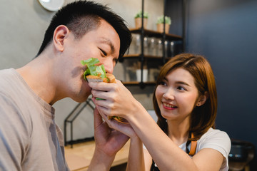 Beautiful happy asian couple are feeding each other in the kitchen. Young asian man and woman have romantic time while staying at home. Couple lifestyle at home concept.