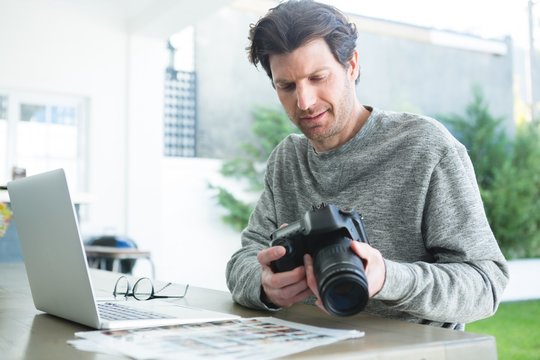 Man using laptop and holding digital camera