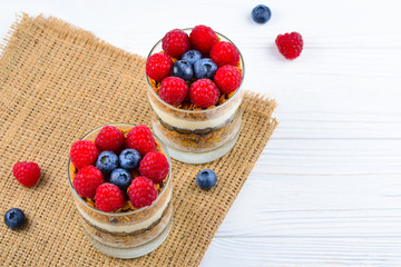 Healthy blueberry and raspberry parfait in a glass on a rustic white wood background. Two portions. Space for text or design.