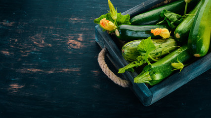 Green zucchini in a wooden box. Fresh vegetables. On a black wooden background. Top view. Copy space.