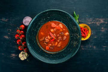 Tomato soup with beef and chili peppers in chervrniy plate. On a wooden table. Top view. Copy space.