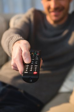 Man changing channel with remote control at home