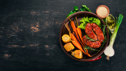 Grilled sausage. Baked Corn and Carrots. On a wooden background. Top view. Copy space.