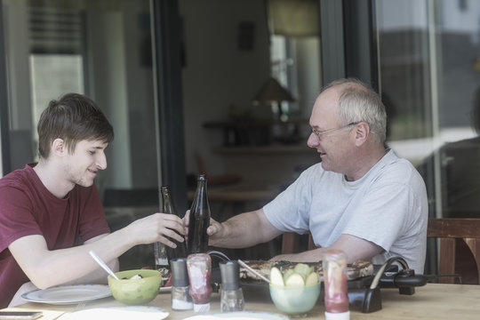 Adult father and son sitting on terrace making a celebratory toast