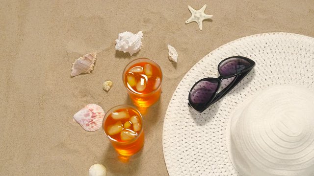 vacation, travel and summer concept - two glasses of aperitif cocktails, sun hat, sunglasses and seashells on beach sand
