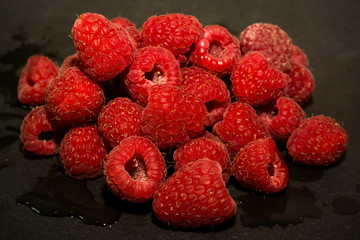 Lot of delicious raspberries on black stone